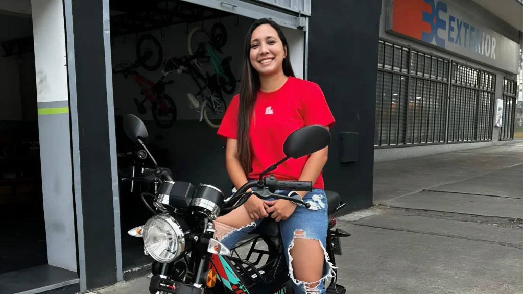 Maieklis Pérez sonriente sobre su nueva motocicleta frente a AVO, celebrando su historia de logro y crecimiento personal.