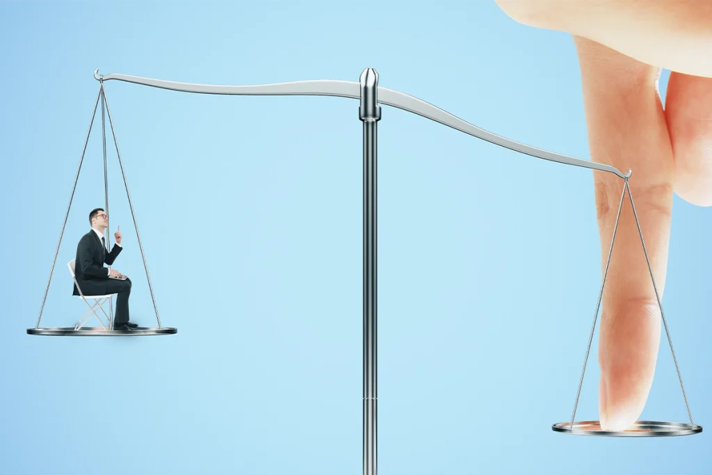 Balance scale comparing a business professional with a laptop against a large finger on a light blue background.