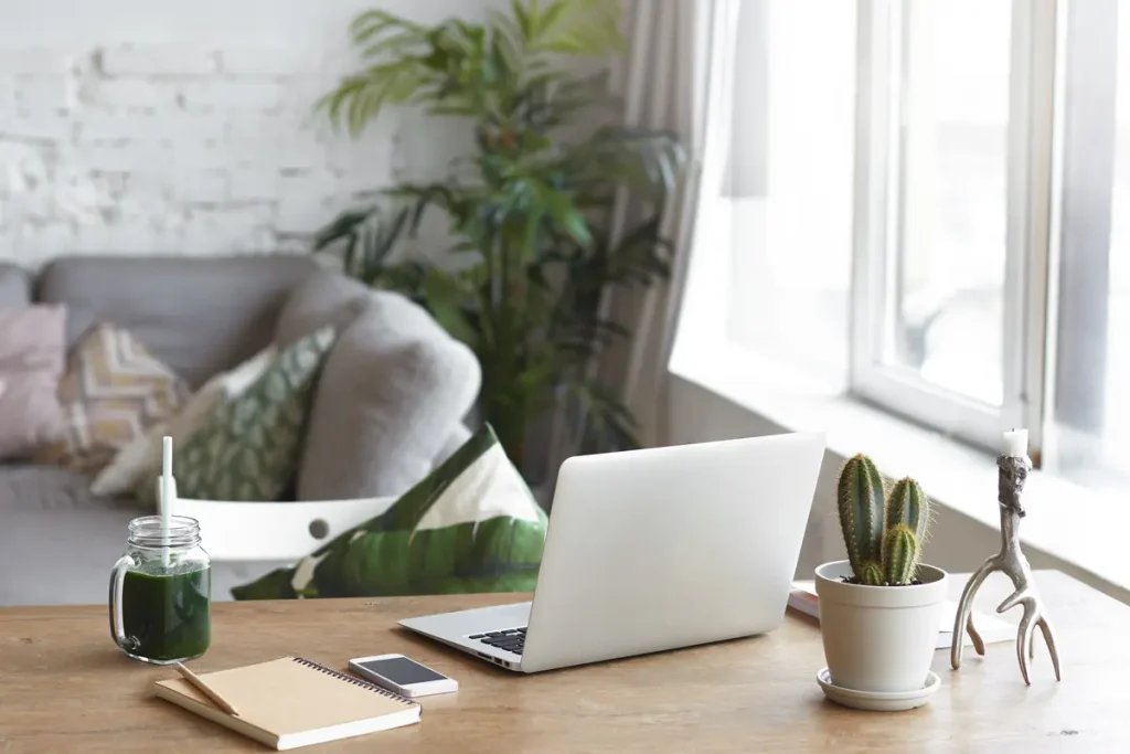 Remote work space desk featuring an open laptop, notebook, smartphone, and a green smoothie.